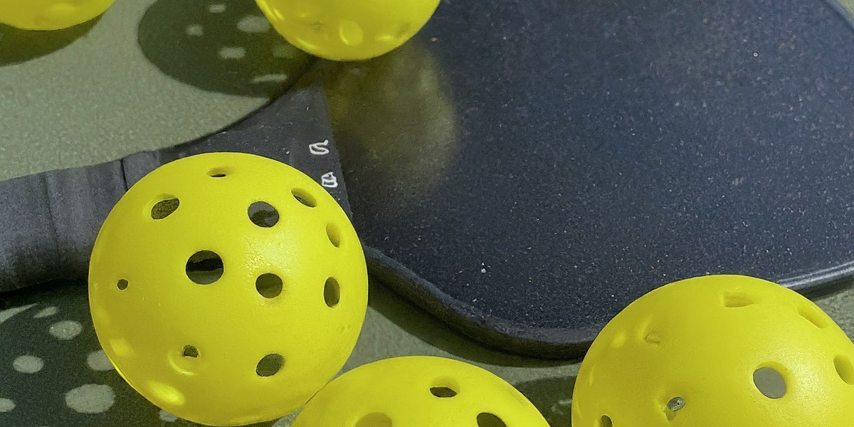 Yellow pickleballs and a plack paddle